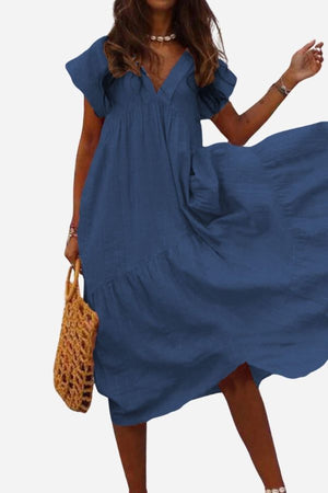 Woman wearing blue V neck tiered cotton midi dress with short sleeves and frill hem carrying wicker handbag