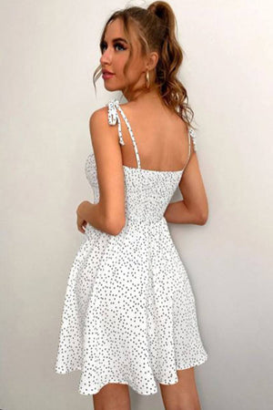 Woman wearing white Bohemian skater dress with black polka dots and sling knot straps, back view