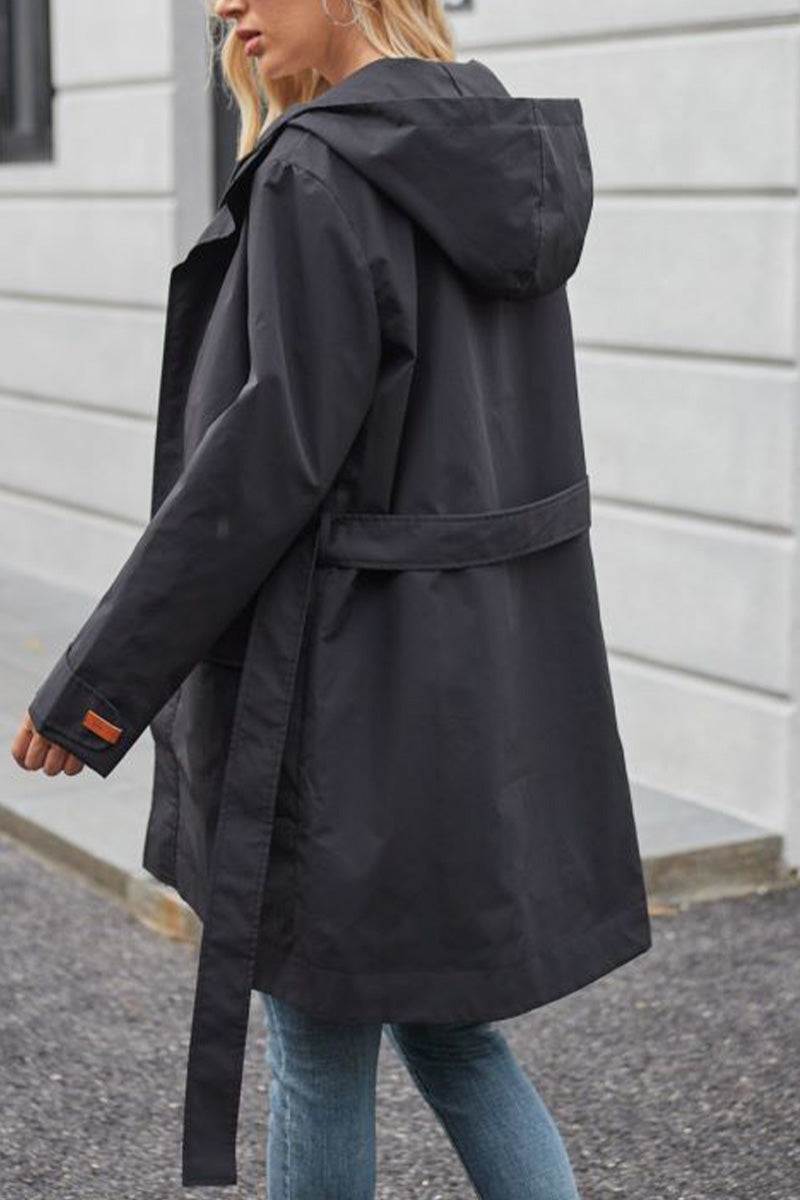 Woman wearing a black water-resistant windbreaker trench jacket with hood and belt outdoors