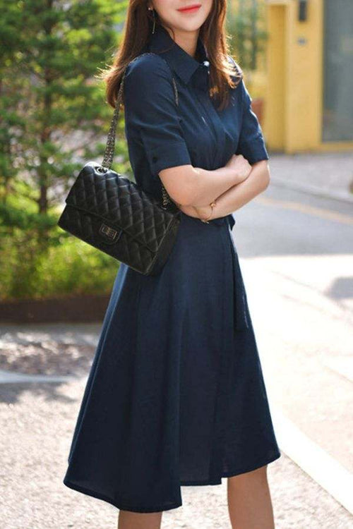 Woman wearing Navy Radiance Belted Shirt Dress with short sleeves and a quilted black handbag outdoors