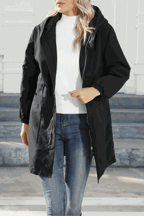 Woman wearing a black lightweight packable water-resistant windbreaker jacket with elastic waist and pockets over a white shirt and jeans