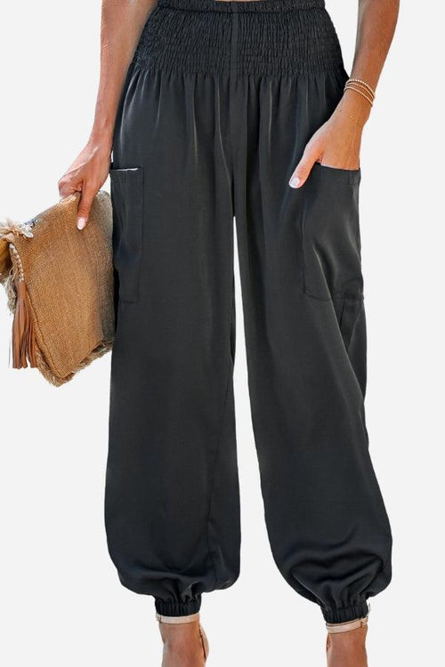Black Boho Dreamer high-waist elastic pants with pockets and cuffed ankles worn by a model holding a straw clutch bag