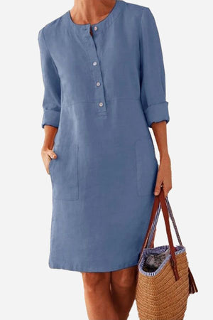 Blue lightweight cotton dress with rolled 3/4 sleeves and front buttons, featuring practical pockets and a knee-length casual fit.