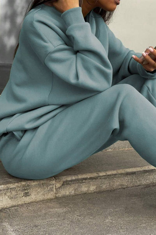 Woman wearing a soft cotton-blended two-piece tracksuit in muted blue sitting outdoors comfortably