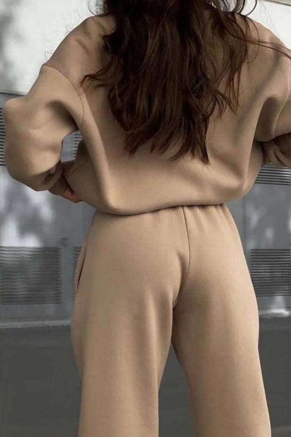 Back view of a woman wearing a beige cotton-blended two-piece tracksuit with long sleeves and high waist pants outdoors.