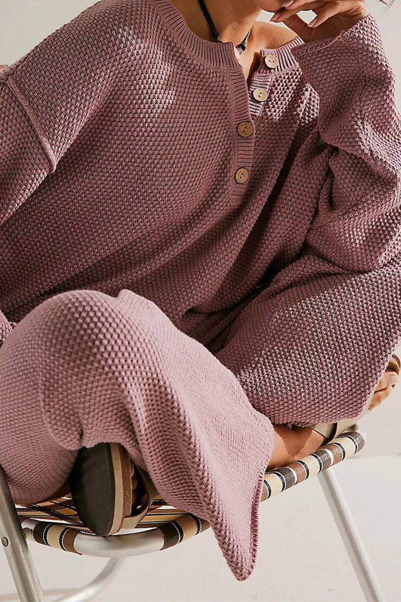 Woman wearing a dusty pink textured knit Multi-Weather Comfort two-piece oversized set with buttons on the top, seated in a woven chair