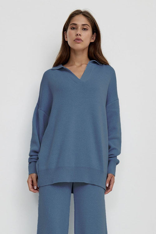 woman wearing plush and preppy camel two-piece set in blue with polo collar pullover and wide-leg pants against white background