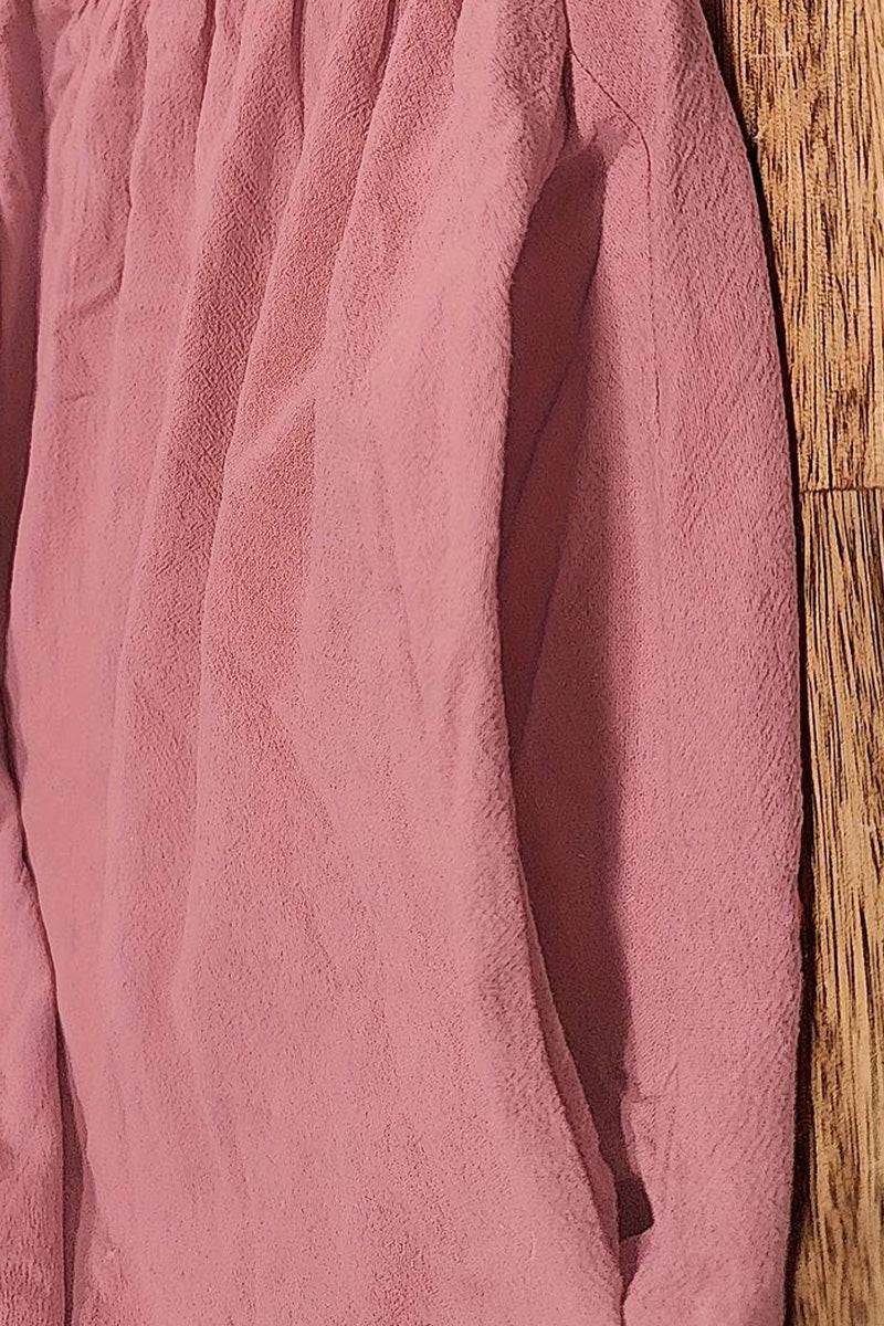 Close-up of pink capped-sleeve voluminous pleated midi dress fabric with pocket detail on wooden floor