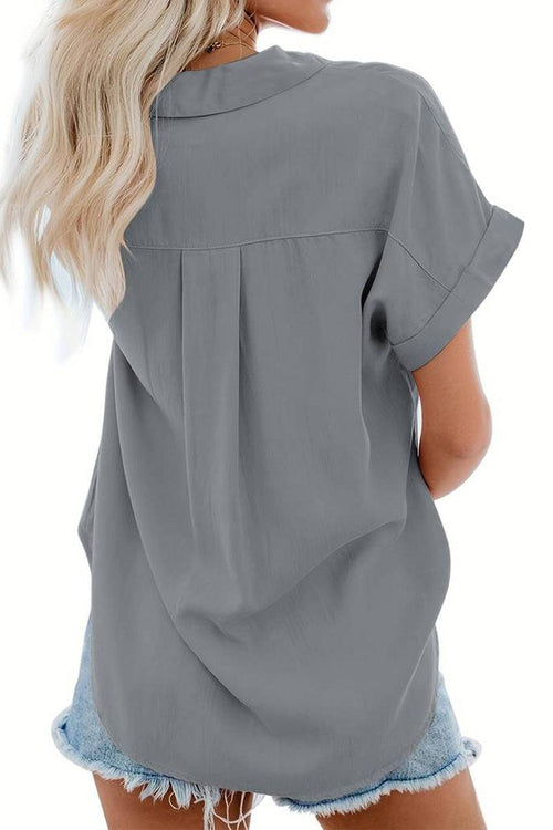 Back view of woman wearing grey V-Neck Collared Button Blouse with rolled short sleeves and denim shorts