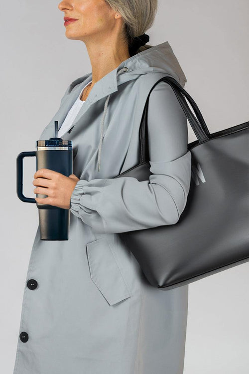 Woman holding indestructible travel cup with handle and secure lid, wearing gray jacket and carrying black tote bag