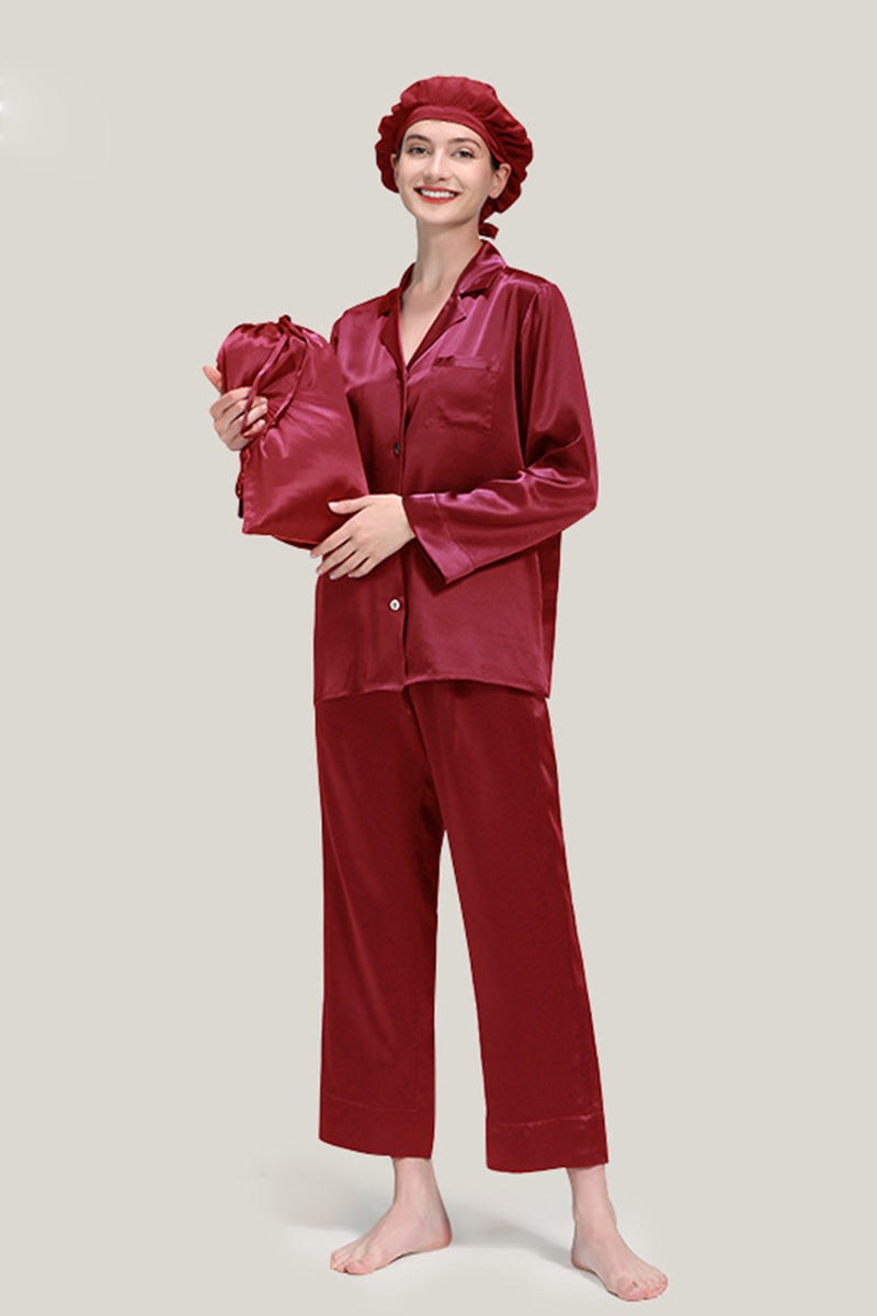 Woman wearing classic burgundy Mulberry Silk Pajama Set with matching sleep cap holding a silk pouch