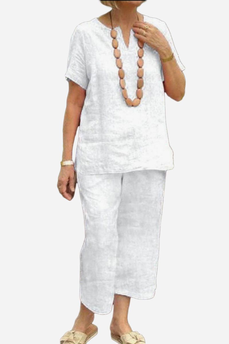 Woman wearing white Breezy Cotton Blend two-piece set with short sleeves and cropped pants, accessorized with a wooden bead necklace and sandals