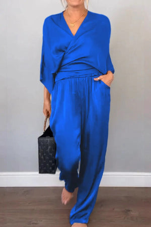 Woman wearing royal blue satin wrap lounge two-piece set with V-neck top and relaxed pants carrying black handbag