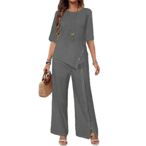 Woman wearing gray Asymmetry Flow Co-ord set with button-front top featuring asymmetrical hem and loose flowing pants, accessorized with necklace and handbag