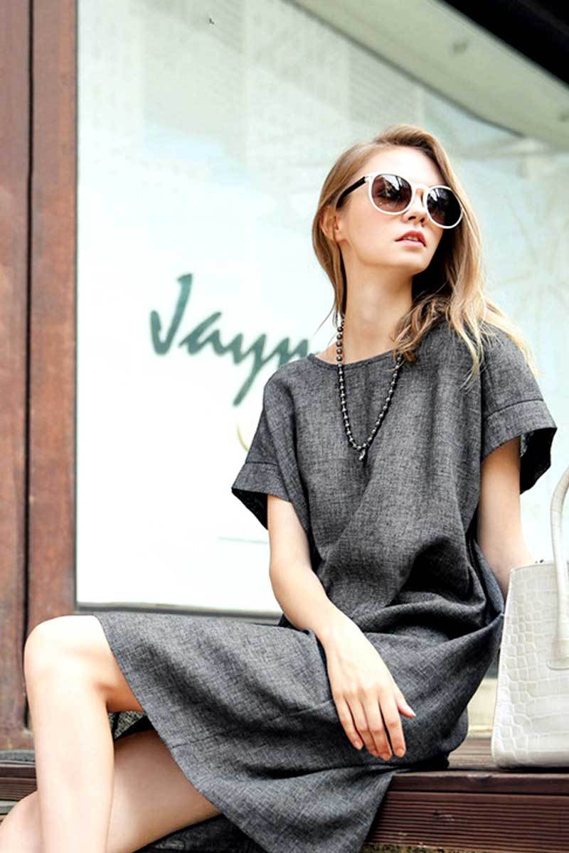 Woman wearing a grey short sleeve shift dress with side pockets and round neck sitting outdoors.