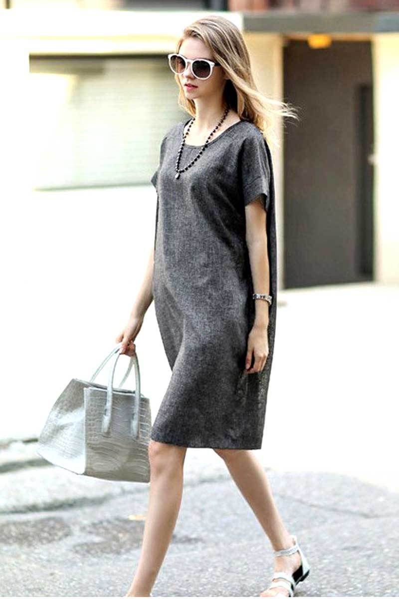 Woman wearing a gray short sleeve shift dress with side pockets, round neck, and above knee length, carrying a gray handbag and wearing sunglasses.