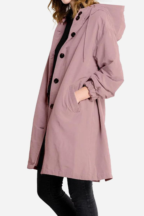 Woman wearing oversized pink water-resistant windbreaker jacket with hood and pockets