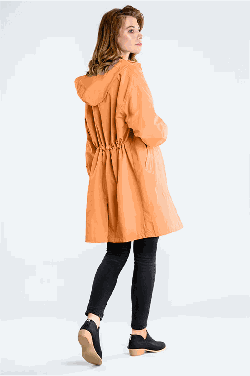 Woman wearing orange water resistant oversized windbreaker with hood and cinched waist from the back