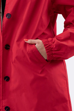 Close-up of hand in pocket of red water-resistant oversized hooded windbreaker rain jacket with button closure and elastic cuff