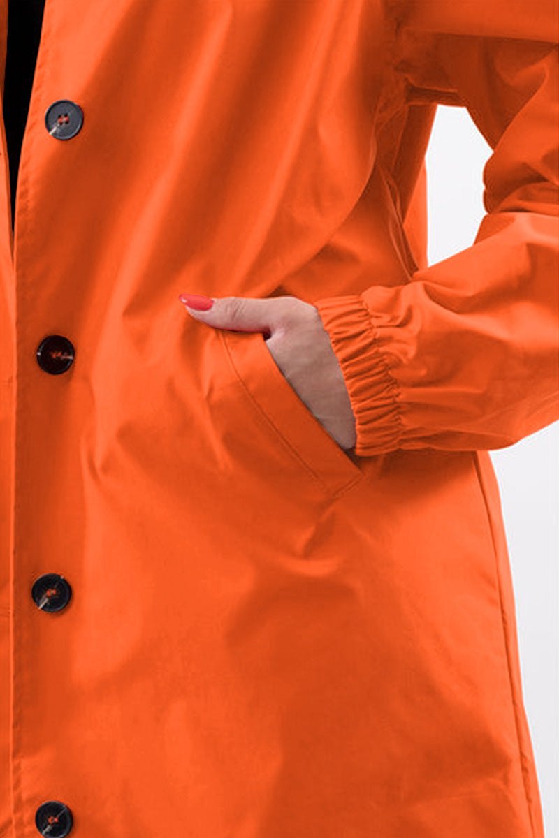 Close-up of orange water-resistant windbreaker with oversized fit and button closure pocket detail