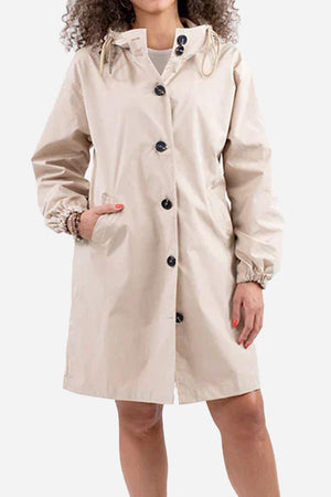 Woman wearing beige water-resistant oversized hooded windbreaker rain jacket with front buttons and pockets