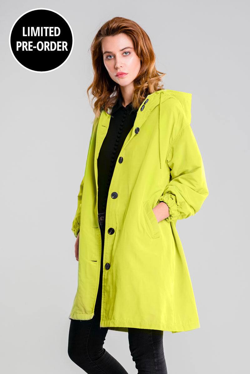 Woman wearing lime green water resistant oversized hooded windbreaker rain jacket with buttons and elastic cuffs
