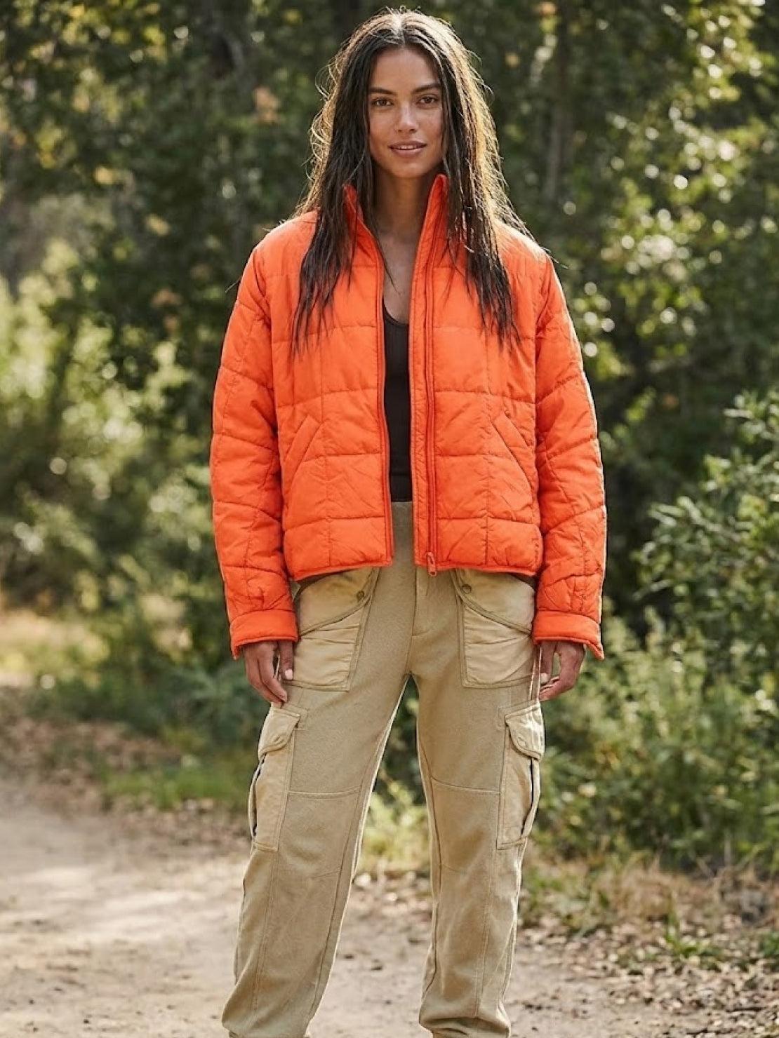 Woman wearing bright orange lightweight puffer travel jacket with beige cargo pants outdoors