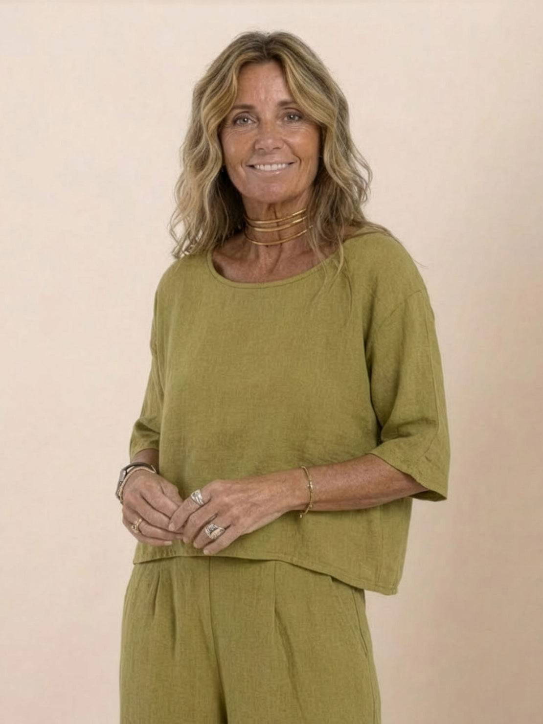 Woman wearing mustard yellow short-sleeved pullover and wide trouser matching set in breathable cotton fabric smiling against beige background