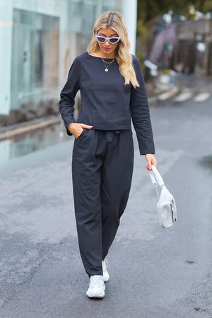 Woman wearing black cotton-linen monochrome relaxed longline top and wide-leg pants walking outdoors with white sneakers and handbag