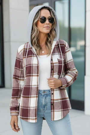 Woman wearing a Highland Plaid Shacket with burgundy and white plaid pattern, gray hood, sunglasses, white top, and light blue jeans outdoors