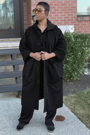 Oversized black water resistant windbreaker jacket with snap buttons and hood worn outdoors