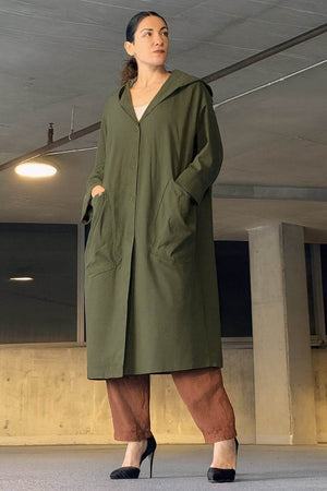 Woman wearing oversized green water resistant windbreaker with hood and front pockets in an indoor setting