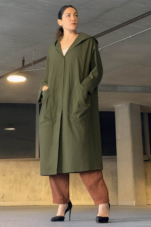 Woman wearing oversized green water resistant windbreaker with hood and front pockets in an indoor setting