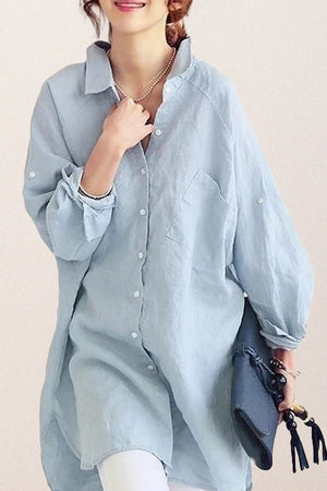 Light blue oversized linen shirt with relaxed fit, button front, and rolled sleeves worn by a woman holding a bag.