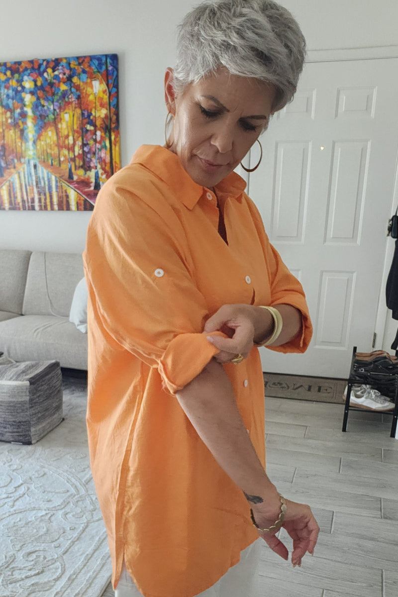 Woman wearing oversized linen shirt in soft orange color with rolled-up sleeves in modern living room setting