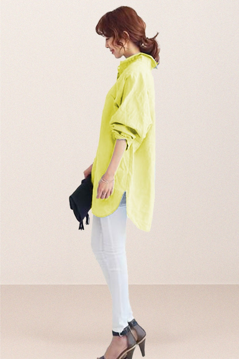 Side view of a woman wearing a light green oversized linen shirt with loose sleeves and a curved hem, paired with white pants and black heels.