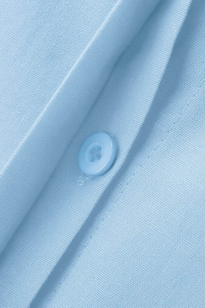 Close-up of oversized 100% cotton light blue shirt fabric with button detail