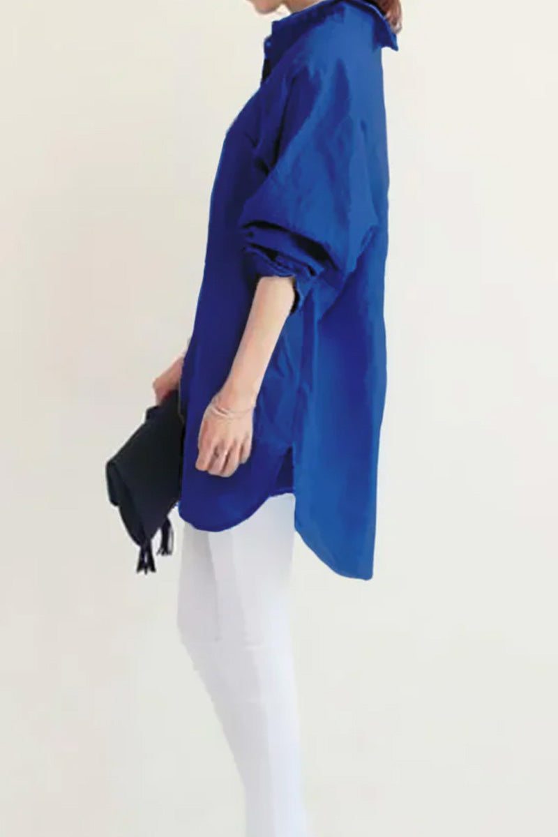 Woman wearing oversized blue linen shirt with rolled sleeves and white pants against plain background