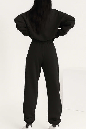 Back view of woman wearing black cotton blend tracksuit with stretch waistband and cuffs, showcasing relaxed fit and minimalist style.