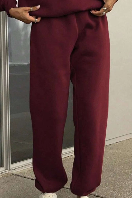 Close-up of burgundy cotton blend tracksuit pants with hands in pockets on a sidewalk