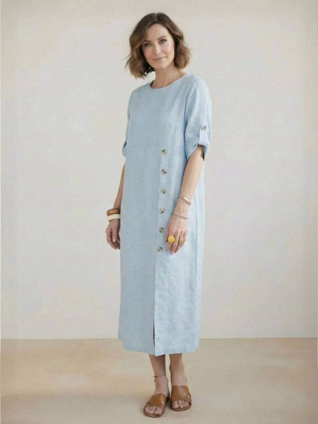 Woman wearing Pure Cotton Elegance dress in white, standing outdoors with green plants background