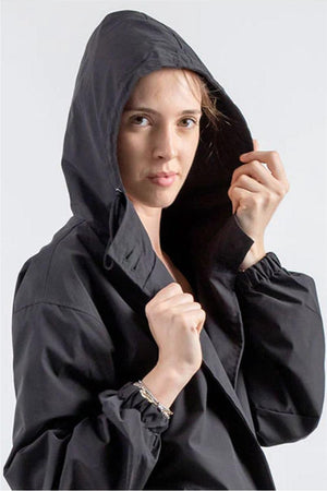 Woman wearing black Rain Couture Windbreaker with hood up, lightweight and water-resistant jacket.