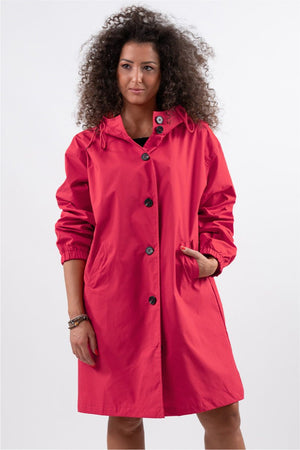 Woman wearing a red Rain Couture Windbreaker oversized, water-resistant jacket with button closure and hood.