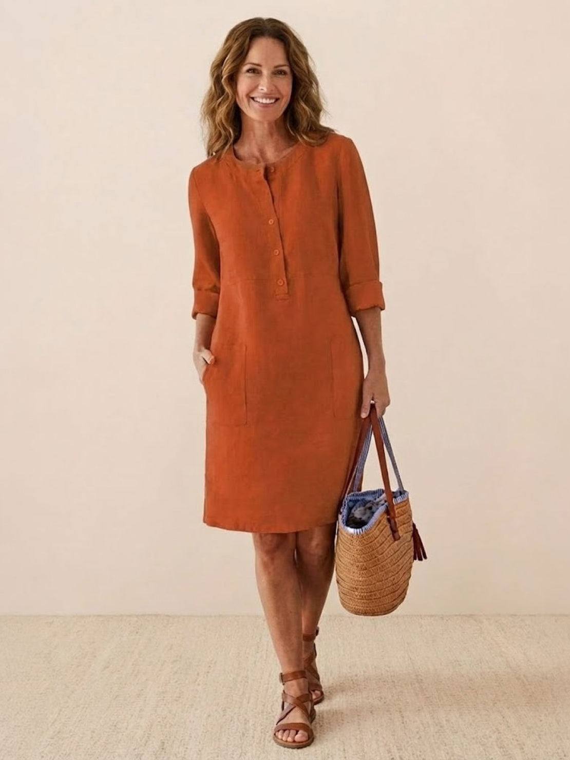 woman wearing rust-colored casual cotton dress with rolled sleeves holding woven handbag