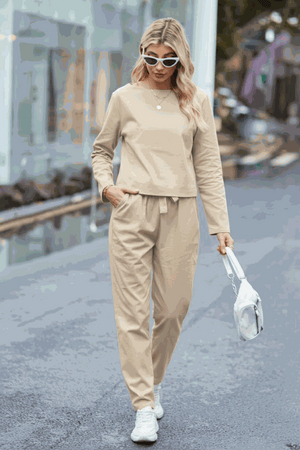 Woman wearing beige cotton-linen monochrome relaxed longline top and wide-leg pants set walking outdoors with sunglasses and white sneakers.