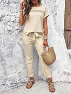 Woman wearing 100% cotton total comfort two-piece beige travel outfit with short sleeves and drawstring pants holding a woven handbag