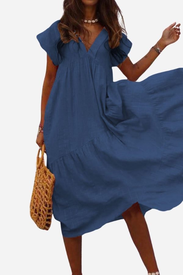 Woman wearing blue V neck tiered cotton midi dress with short sleeves and frill hem carrying wicker handbag