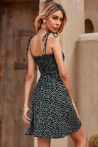 Woman wearing black bohemian skater dress with white polka dots and sling knot straps outdoors