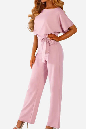 Woman wearing chic short-sleeved wide-leg pink jumpsuit with belt and high waist
