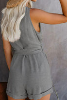 Back view of woman wearing a sleeveless grey Alluring V-neck Layered Romper with high waist and belt detail.